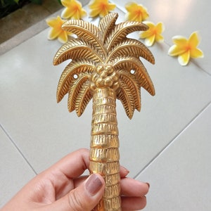 Puede incluir: Un tirador de puerta de palmera dorado con un diseño detallado. El tirador está hecho de latón macizo y tiene un acabado liso y pulido.