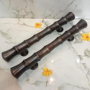 May include: Two dark bronze door handles featuring a textured bamboo-inspired design with distinct nodes along the length of each handle. Each handle is mounted on two circular bases and has a smooth, metallic finish with subtle dark brown highlights.