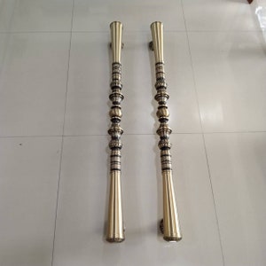 May include: A pair of ornate gold door handles with intricate details and a black finish. The handles are long and slender, with a rounded top and a decorative base.