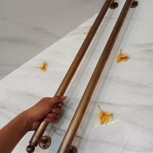 May include: Two bronze door pull handles with a rounded design. Each handle has a circular base and a cylindrical bar. The handles are displayed on a white marble surface with yellow flower petals.