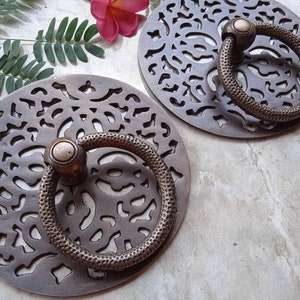 Pode incluir: Duas puxadores de porta redondos, ornamentados, de latão com um design decorativo recortado. Cada puxador tem uma alça de anel com uma maçaneta redonda.