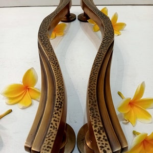 May include: A pair of antique brass door handles with a wavy design. The handles have a hammered texture and are finished in a warm, aged brass tone.