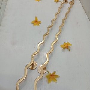May include: Two gold wavy door handles with round bases. CENTRAL BRASS BALI is written in the bottom right corner of the image.