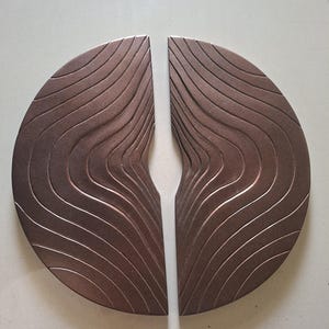 May include: A pair of semi-circular door handles in a metallic bronze finish. Each handle features a series of deep, flowing, wave-like grooves carved into the surface, creating a textured pattern that mimics natural topographical lines.
