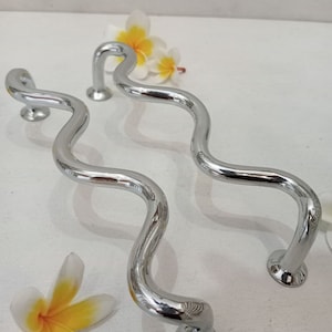 May include: Two silver wavy door handles with a polished finish. The handles are on a white surface with two white flowers.