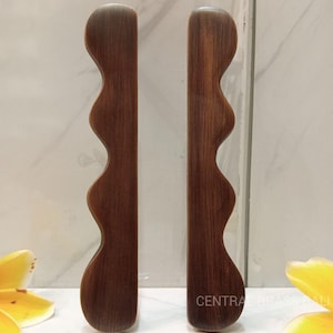 Puede incluir: Dos tiradores de armario de color bronce con un diseño ondulado y orgánico. Los tiradores están orientados verticalmente y tienen un acabado liso y pulido. El texto "CENTRAL BRASS BALL" es visible en el tirador derecho.