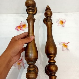 May include: Two antique brass door handles with a decorative, ornate design. The handles have a warm, golden-brown color and a classic, vintage aesthetic. The handles are displayed with several pink and yellow flowers.