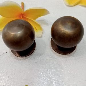 May include: Two round, brass cabinet knobs with a smooth, aged finish. The knobs are slightly different sizes and are shown on a white surface.