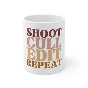 Könnte beinhalten: Weiße Keramiktasse mit dem Text "SHOOT CULL EDIT REPEAT" in Braun, Rosa und Orange.