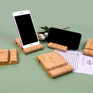 May include: Four wooden phone stands made of bamboo. The stands are in various positions, with one stand holding a smartphone. The stands are on a green surface.