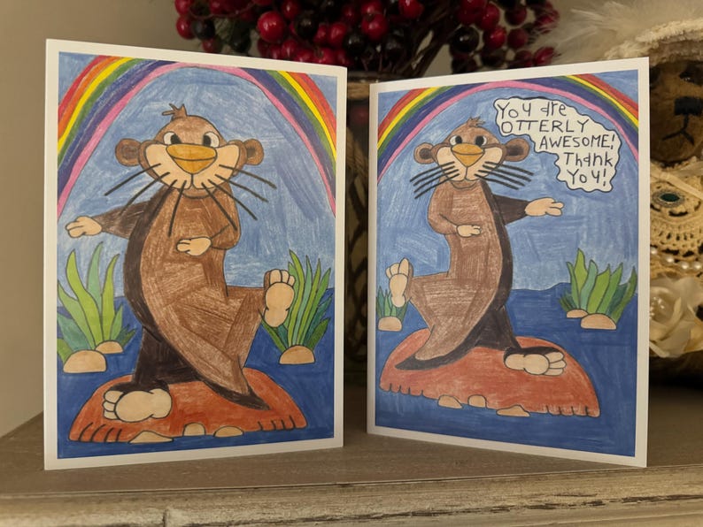 Puede incluir: Dos tarjetas de felicitaci&oacute;n con una nutria de dibujos animados en cada una. La nutria es marr&oacute;n y tiene un arco&iacute;ris detr&aacute;s. El texto de la tarjeta dice "&iexcl;Eres totalmente incre&iacute;ble! &iexcl;Gracias!"
