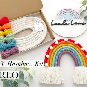 Peut inclure: Kit de fabrication de rainbow DIY avec du fil coloré et de la corde blanche dans une boîte. L'arc-en-ciel fini est réalisé avec le fil et la corde et a des pompons blancs sur le dessus.