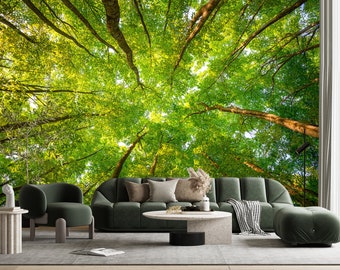 May include: A living room interior design with a green sofa and armchair, a coffee table, and a throw blanket. The wall is a mural of a lush green forest canopy viewed from below.