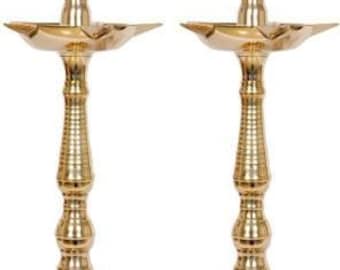 Op de afbeelding: Twee gouden metalen olielampen met een traditioneel ontwerp. Elke lamp heeft een ronde basis, een lange, slanke steel en een ronde kom aan de bovenkant. De lampen zijn perfect om elke woning een vleugje elegantie te geven.