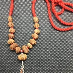 May include: A red string necklace with brown wooden beads and a silver pendant. The necklace is on a black textured surface.