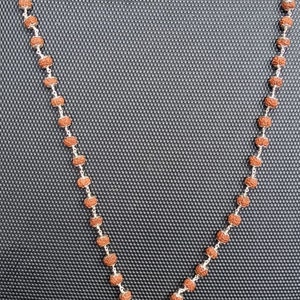 May include: A brown and silver mala necklace with a tassel. The necklace is made of small, round beads and is strung on a silver chain.