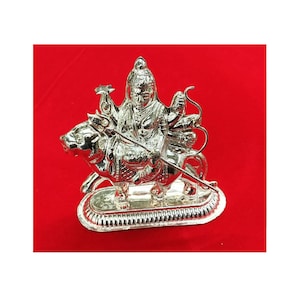 May include: Silver statue of a Hindu deity riding a bull. The deity has multiple arms and is holding a weapon in each hand. The statue is on a silver base.
