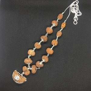 May include: A silver chain necklace with brown wooden beads and a silver pendant featuring a symbol. The necklace is displayed against a black backdrop.