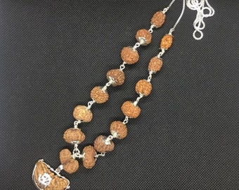 May include: A silver chain necklace with brown wooden beads and a silver pendant with a symbol. The necklace is on a black background.