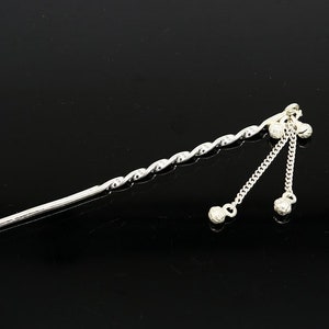 May include: Silver hair stick with a twisted design and three dangling balls at the end.