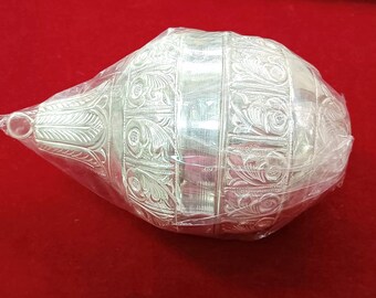May include: A silver, intricately engraved, decorative, egg-shaped container with a small handle. The container is wrapped in clear plastic.