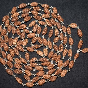 May include: A brown wooden mala necklace with silver beads and a tassel. The necklace is made of rudraksha beads, which are believed to have spiritual and healing properties.