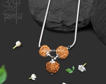 May include: A silver chain necklace with three brown rudraksha beads. The beads are connected by silver links. The necklace is on a black background with white flowers.