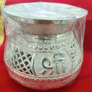 May include: A silver decorative bowl with intricate designs and a raised rim. The bowl features a raised "Om" symbol in the center.