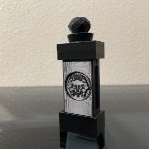 May include: A black and silver decorative pillar with a geometric design on top. The pillar has a raised, circular design with the word "FUNK" in the center.