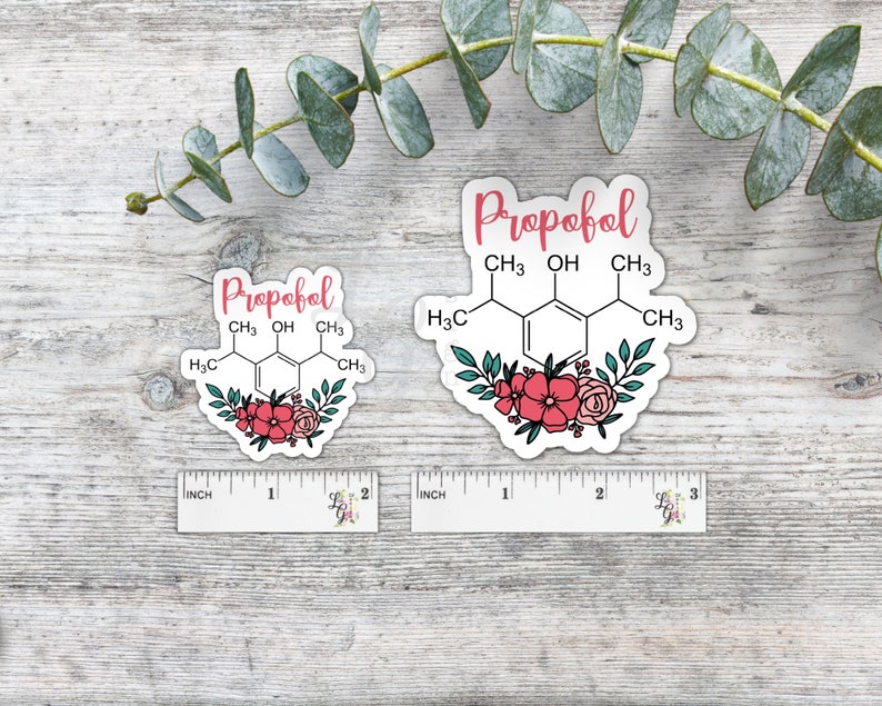May include: Two white stickers with floral designs and the chemical formula for Propofol. The stickers are on a wooden surface.