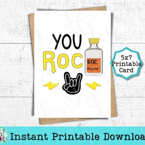 Może przedstawiać: Drukowana karta 5x7 z białym tłem i tekstem "YOU ROC" w kolorze żółtym i czarnym. Obok tekstu znajduje się mały, kreskówkowy flakon z tekstem "ROC 10 mg/ml". Pod tekstem znajduje się czarny gest rock and roll z dwoma żółtymi błyskawicami.