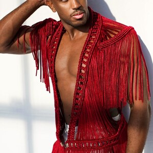 May include: A red crocheted vest with fringe detailing. The vest has a deep V-neck and is open in the front.