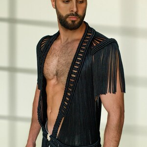 May include: A black fringe vest with a deep V-neckline. The vest is made of a woven material and has a fringe trim around the edges.