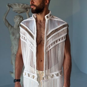May include: A white crocheted vest with a fringe hem and gold accents. The vest is sleeveless and has a high neckline.