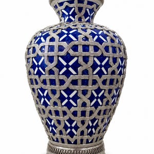Peut inclure: Un vase décoratif doté d'un corps bleu profond avec des accents géométriques blancs, recouvert d'un treillis métallique argenté complexe. Le récipient présente un col évasé et une base circulaire, tous deux ornés d'une fine bordure perforée.