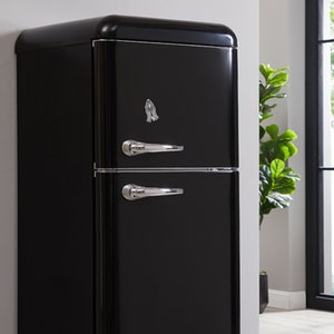 K&ouml;nnte beinhalten: Ein schwarzer Retro-K&uuml;hlschrank mit zwei T&uuml;ren und silbernen Griffen. Der K&uuml;hlschrank hat ein Gebets-Hand-Design auf der oberen T&uuml;r.