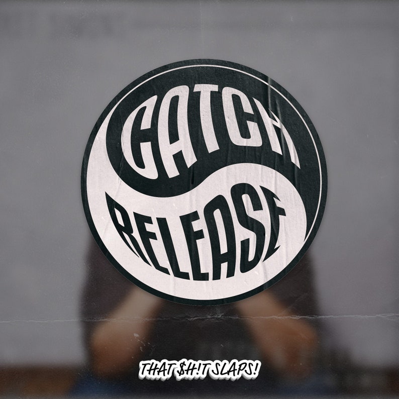 May include: Black and white yin yang symbol with the words "CATCH RELEASE" in a bold, stylized font. The text "THAT $#!T SLAPS!" is below the symbol.