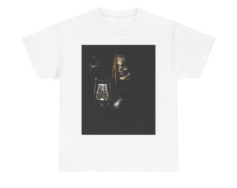 May include: White t-shirt with a dark image of a person in a mask holding a lantern. The mask has a detailed design with visible teeth. The lantern is lit, creating a glow in the dark background.