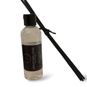 May include: A black glass bottle with a black label that reads "Graveyard Moss Reed Diffuser" and directions for use. The bottle is filled with a clear liquid and has black reeds sticking out of the top.
