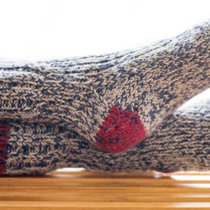 Puede incluir: Un par de calcetines acogedores de punto con un patrón gris y blanco y detalles rojos. Los calcetines están hechos de un hilo grueso y cálido y tienen un ajuste cómodo.
