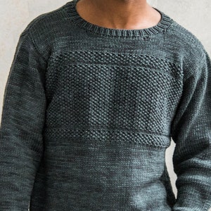 May include: A dark green sweater with a textured pattern on the chest. The sweater has a crew neck and long sleeves.