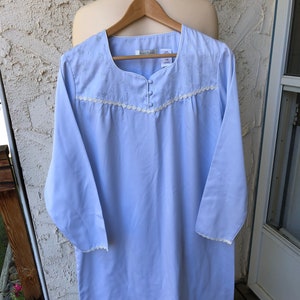 May include: A light blue nightgown with white lace trim and embroidered flowers. The nightgown has a button closure at the neckline and long sleeves. The label reads "Kay Ann".