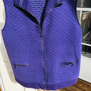 Peut inclure: Un gilet matelassé violet avec une fermeture éclair et deux poches. Le gilet est doublé d'une bande rayée.