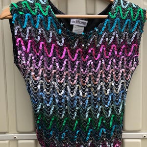 May include: A sleeveless sequined top with a rainbow chevron pattern. The top is black with sequins in shades of pink, blue, green, and silver. The label on the top reads "editions".