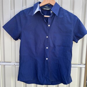 May include: A navy blue short-sleeved shirt with a white collar and white buttons, hanging on a wooden hanger. The label shows the brand name "Eddie Bauer". The shirt is a classic style.