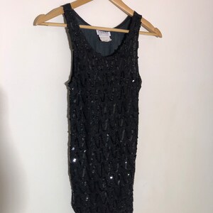 May include: A black sleeveless sequined top with a scoop neck. The top is made of a soft, stretchy fabric and is covered in sequins. The top has a relaxed fit and is perfect for a night out.