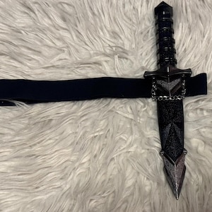 May include: A black leather belt with a silver chain and a black dagger with a silver tip.