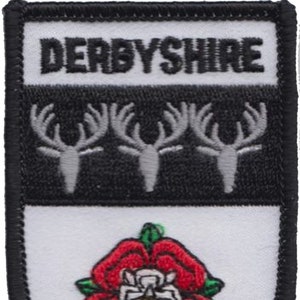 May include: A black and white embroidered patch with the text "DERBYSHIRE" in white. The patch features three white deer antlers on a black background and a red rose with a white centre on a white background.