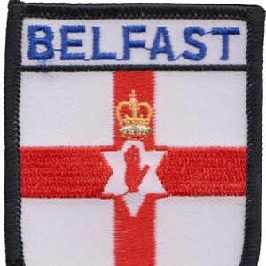 May include: A black and white embroidered patch with the word "BELFAST" in blue lettering. The patch features the flag of Northern Ireland, which includes a red cross on a white background with a red hand and a gold crown in the center.