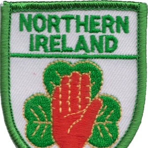 Puede incluir: Un parche bordado verde y blanco con las palabras "Northern Ireland" y una mano roja dentro de un trébol verde.